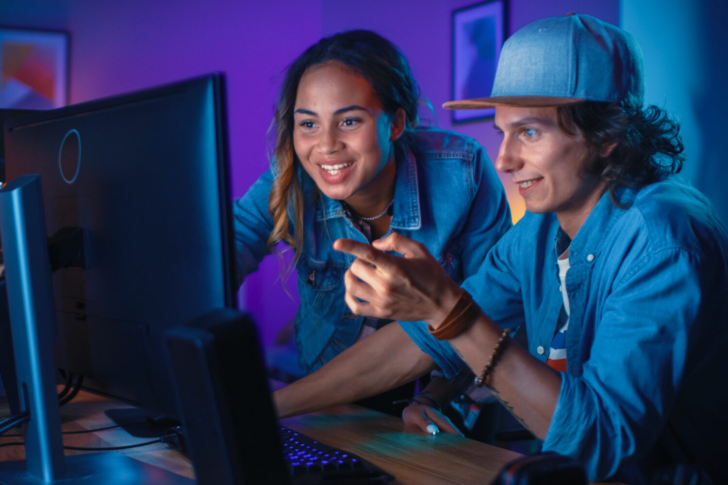 Pretty Black Girl Actively Talks and Explains Something to Her Friend and Points on a Computer Screen. They Have a Discussion about New Creative Ideas. Cozy Room is Lit with Warm and Neon Light.