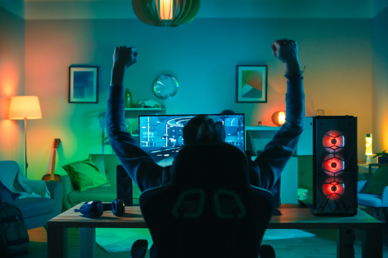 Back Shot of a Gamer Playing and Winning in First-Person Shooter Online Video Game on His Powerful Personal Computer. Room and PC have Green Neon Led Lights. Cozy Evening at Home.