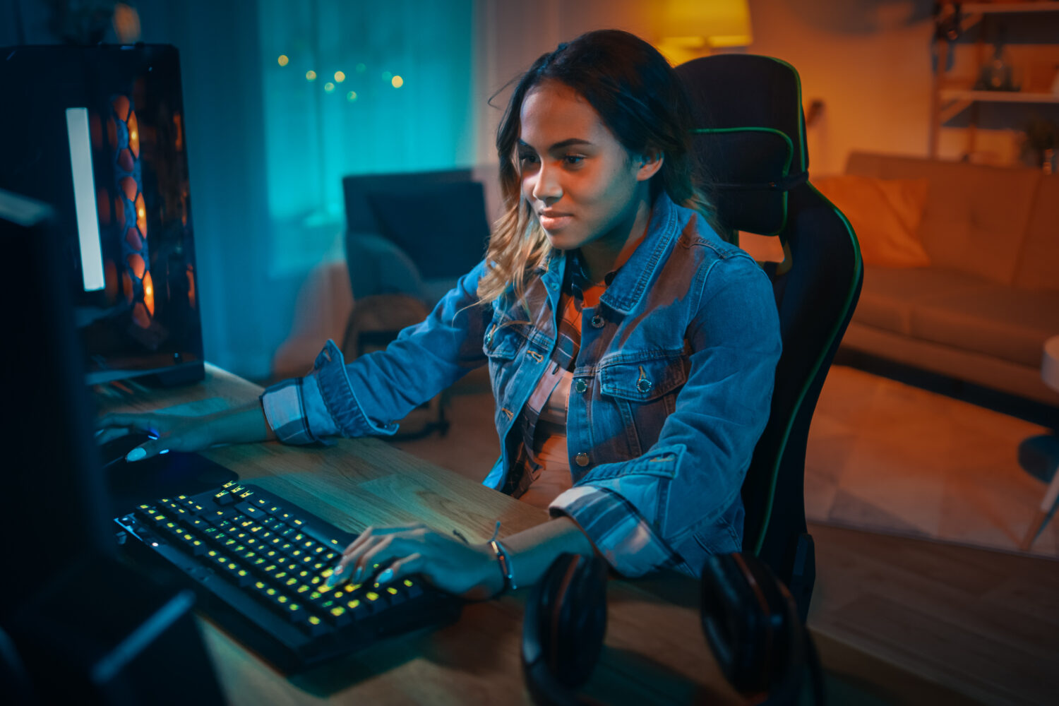 Excited and Pretty Black Gamer Girl is Playing Online Video Game on Her Personal Computer. Room and PC have Colorful Warm Neon Led Lights. Cozy Evening at Home.